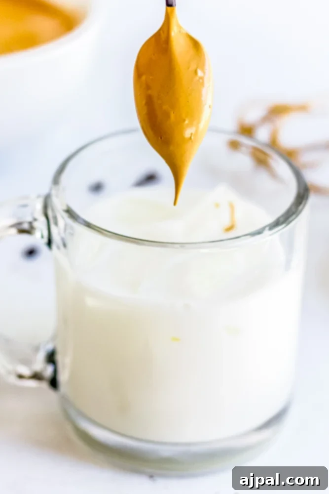 Golden coffee foam being gently spooned onto a glass of milk.