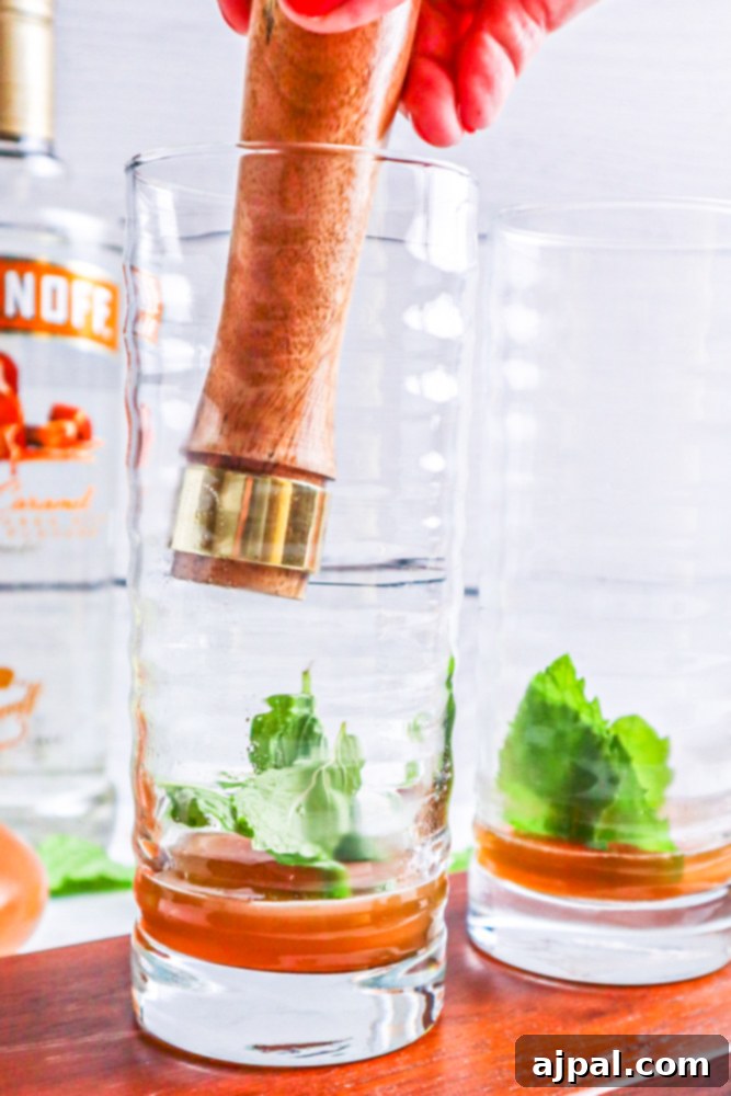 A person is muddling mint leaves in a glass with simple syrup to make an Apple Cider Mojitos Cocktail Recipe.