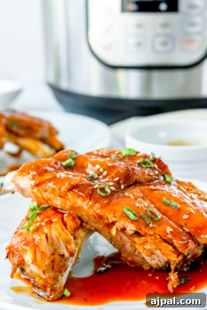 Instant Pot Sticky Asian BBQ Ribs 2 Perfectly cooked Instant Pot Asian BBQ Ribs coated in a vibrant orange sauce and garnished with fresh green onions.