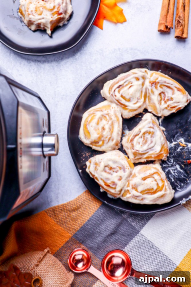 Irresistible pumpkin cinnamon rolls in a black pan, perfectly baked in an Instant Pot, resting on a elegant marble table beside a checkered kitchen towel.