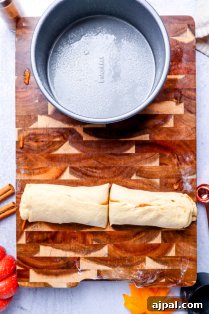 A roll of dough on a wooden cutting board, neatly cut in half, with a metal cake pan visible in the background.