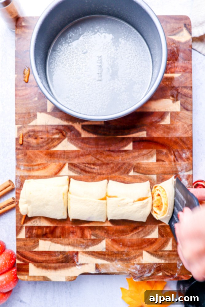 A roll of dough on a wooden cutting board, now precisely cut into four pieces, with a metal cake pan waiting in the background.
