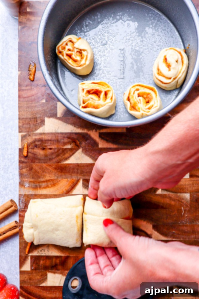Precisely cut pieces of the rolled dough being carefully placed into a metal cake pan, with their characteristic swirls beautifully exposed.