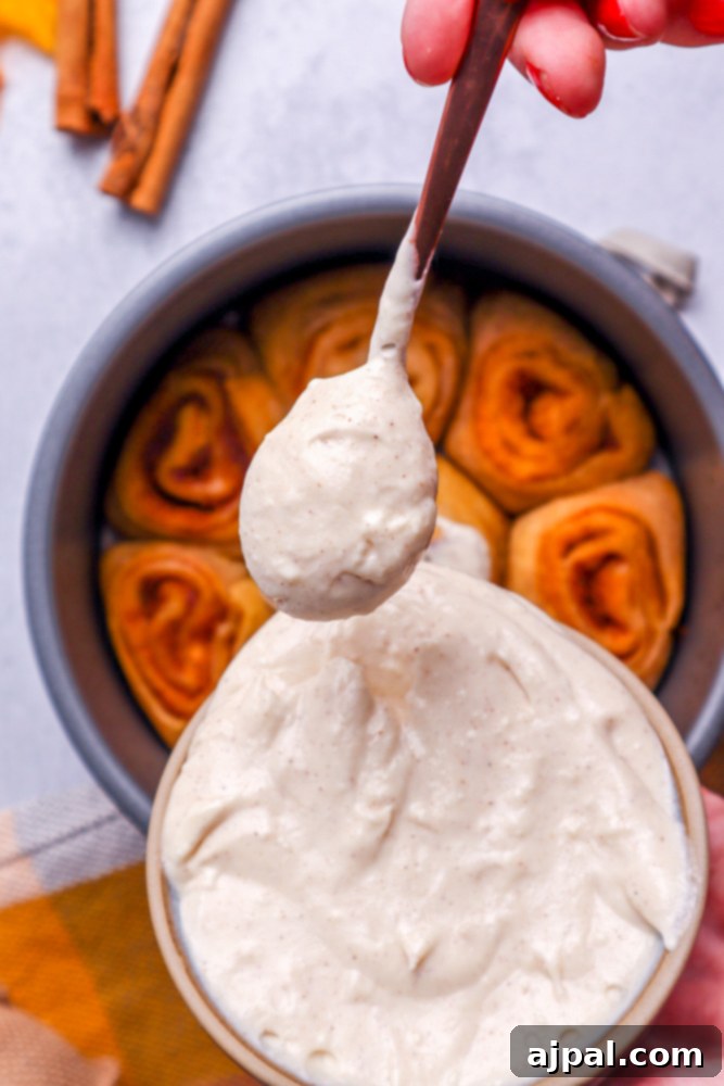 Warm cinnamon rolls nestled in a metal cake pan, with a bowl of luscious white frosting positioned invitingly in front, ready to be spooned on.