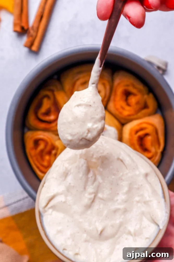 Easy Instant Pot Pumpkin Cinnamon Rolls 18 cinnamon rolls in a metal cake pan with white frosting in the front ready to spoon on