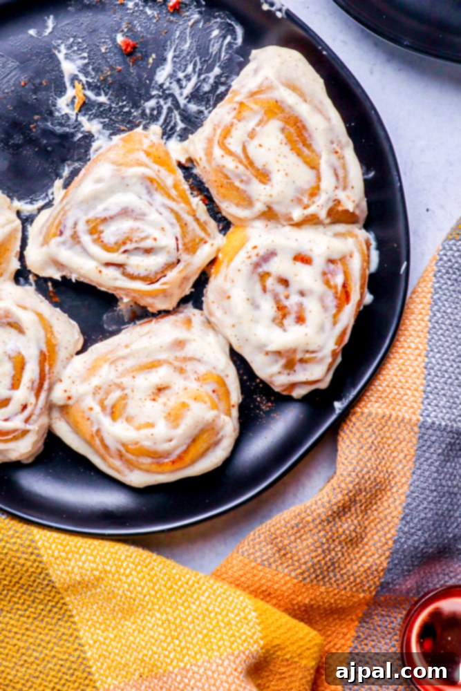 Fluffy pumpkin cinnamon rolls resting in a black pan, accompanied by a warm checkered hand towel in classic fall colors.