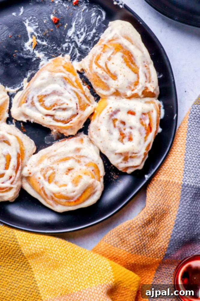 Easy Instant Pot Pumpkin Cinnamon Rolls 20 pumpkin cinnamon rolls sitting in a black pan with a checkered fall color hand towel