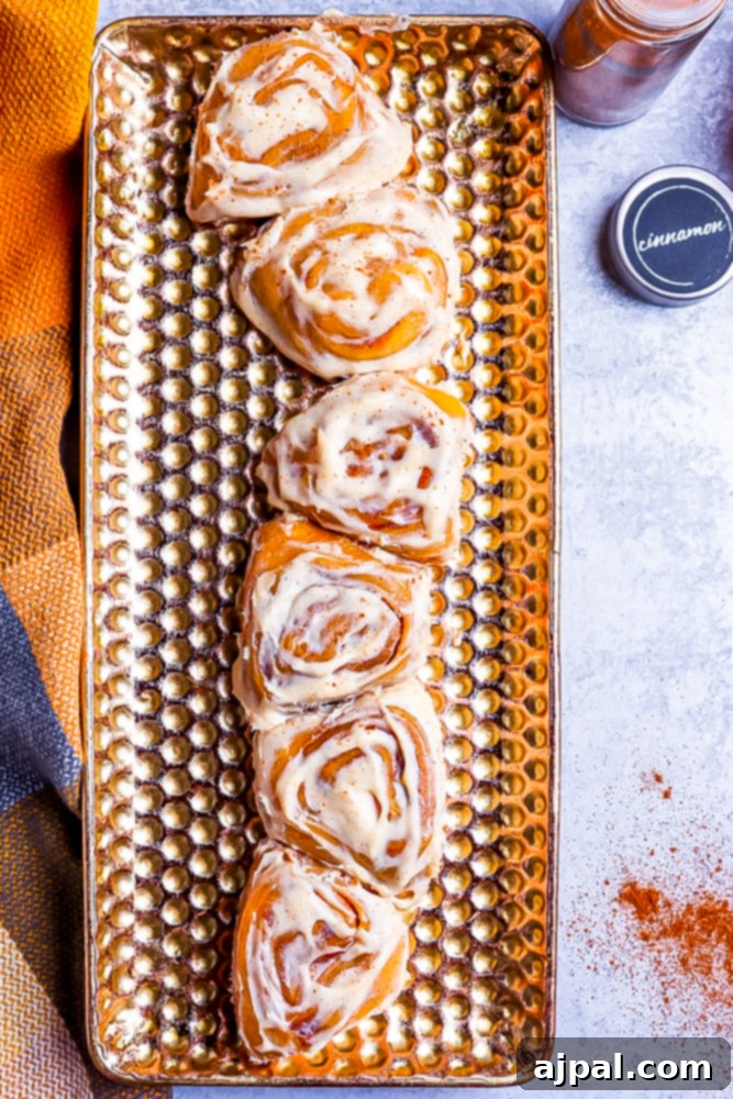 Golden-baked pumpkin cinnamon rolls elegantly arranged on a perforated golden plate, with a hint of cinnamon in the background on a marble surface.