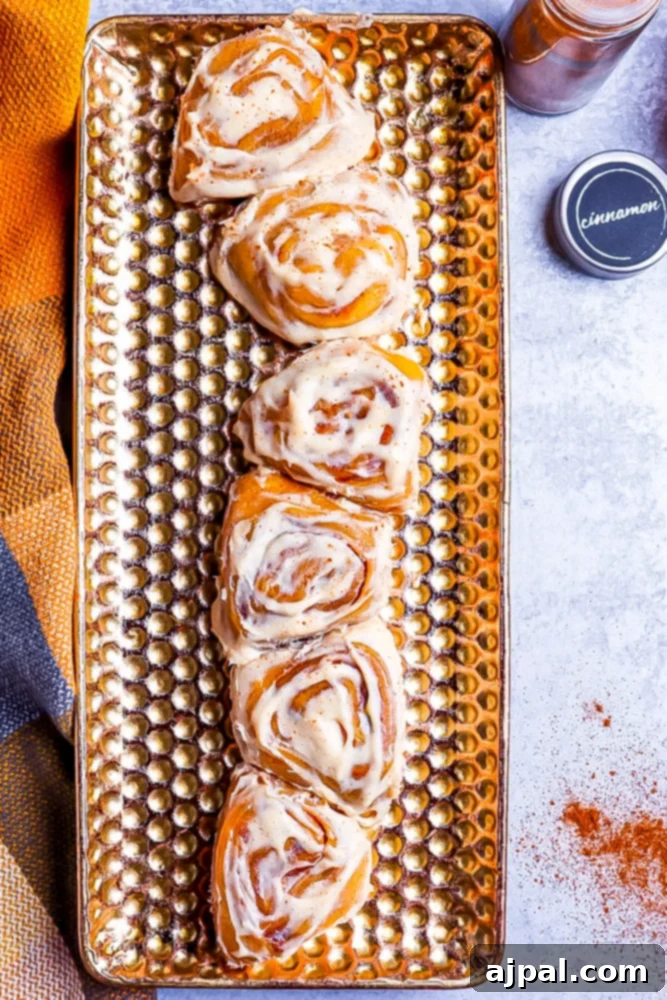 Easy Instant Pot Pumpkin Cinnamon Rolls 3 pumpkin cinnamon rolls sitting longways on a golden plate that has lots of perforations. Cinnamon in the background on a marble table