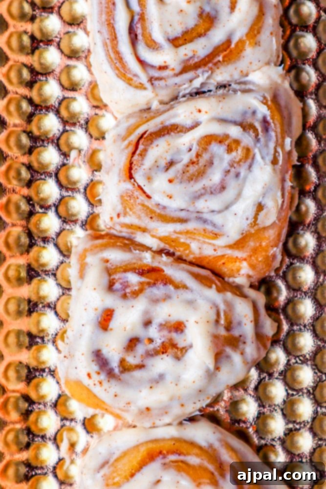 Easy Instant Pot Pumpkin Cinnamon Rolls 4 pumpkin cinnamon rolls sitting longways on a golden plate that has lots of perforations.