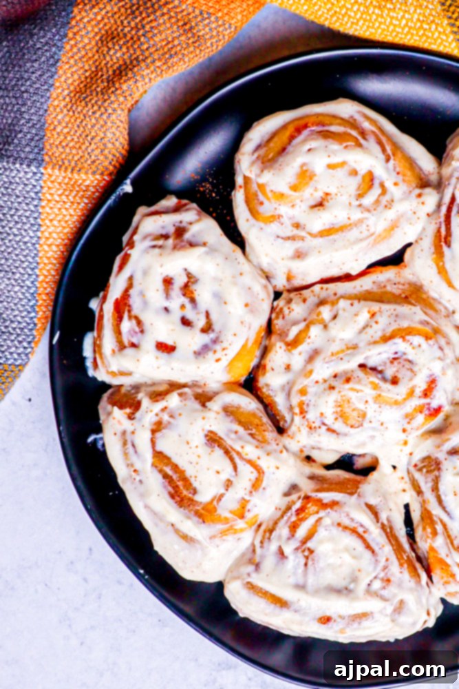 A captivating close-up of pumpkin cinnamon rolls on a black plate, showcasing their inviting golden-brown crust and spiral filling.