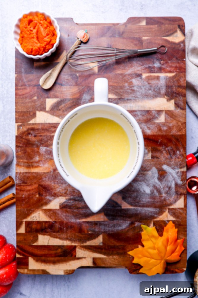 Melted butter in a white measuring cup on a rustic wooden cutting board, ready for the next step.