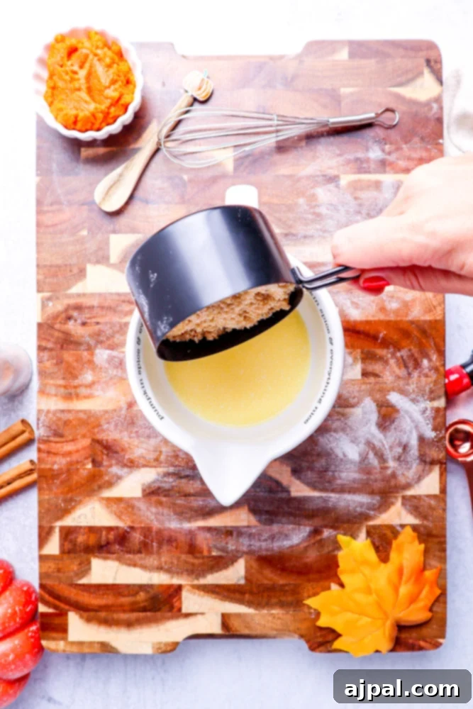 Easy Instant Pot Pumpkin Cinnamon Rolls 7 melted butter in a white measuring cup with brown sugar being poured in on a wooden cutting board