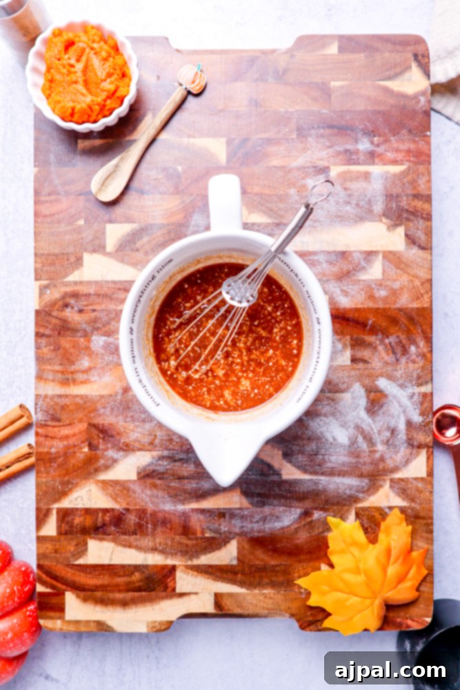 A mix of melted butter and brown sugar swirls in a white measuring cup on a wooden cutting board.
