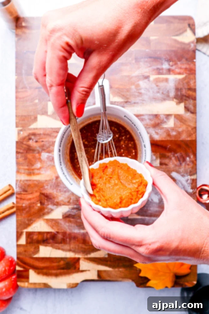 Easy Instant Pot Pumpkin Cinnamon Rolls 9 melted butter and brown sugar in a white measuring cup with spices being added from a white bowl on a wooden cutting board