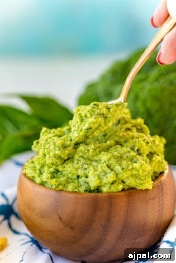 A wooden bowl filled with bright green broccoli pesto, accompanied by a wooden spoon, showcasing a delicious and healthy recipe for broccoli pesto.