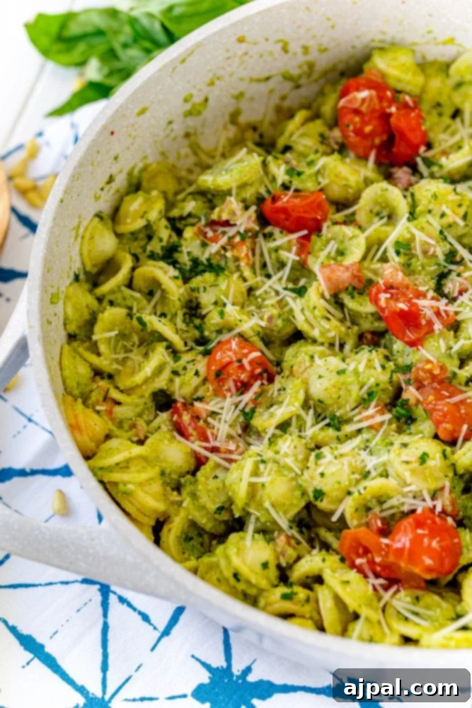 A serving of pasta with fresh broccoli pesto, cherry tomatoes, and grated parmesan cheese, cooked in a skillet.