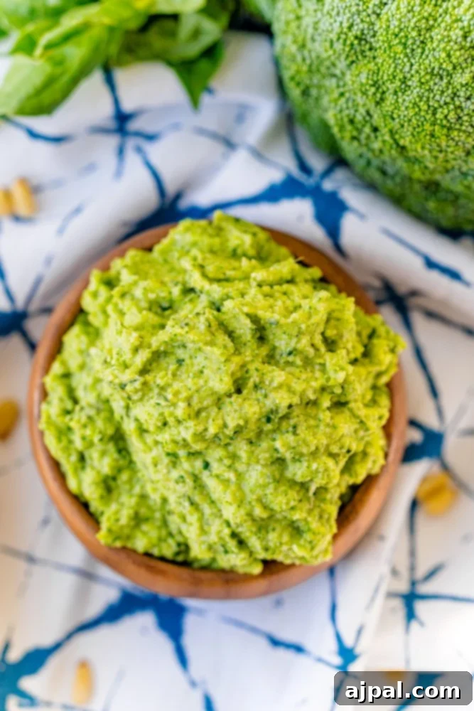 A beautifully presented bowl of bright green broccoli pesto rests on a blue tablecloth, highlighting the vibrant color and delicious texture of this easy recipe.