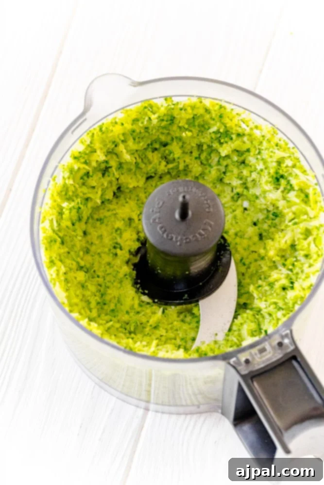 A close-up view inside a food processor, showing the initial stages of making a simple broccoli pesto with blended broccoli florets.