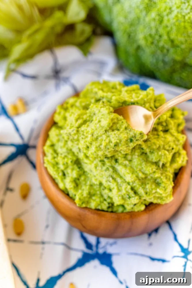 A rustic wooden bowl filled with freshly made broccoli pesto, with a spoon resting in it, ready to be served.