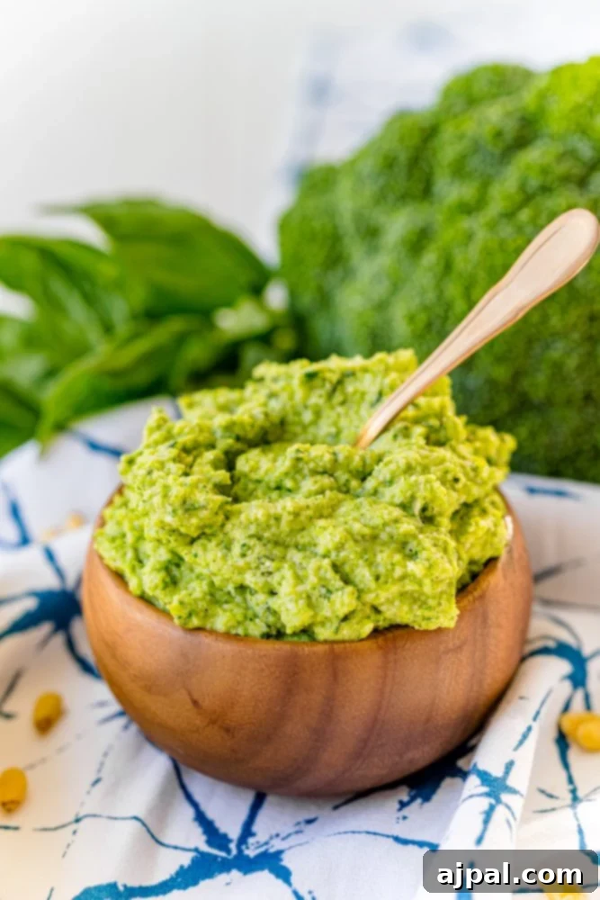 A wooden bowl filled with vibrant green broccoli pesto, accompanied by a wooden spoon, showcasing an easy and delicious recipe.