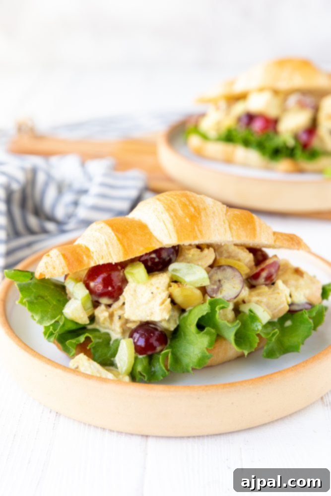 Chicken salad croissant sandwich on a plate with grapes and lettuce