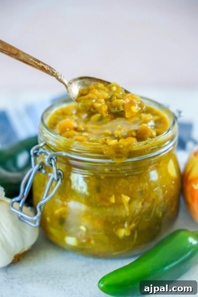 A jar of vibrant green chile sauce with a spoonful of the sauce in front, ready to be enjoyed. The deep green hue suggests the richness of roasted Pueblo chiles.