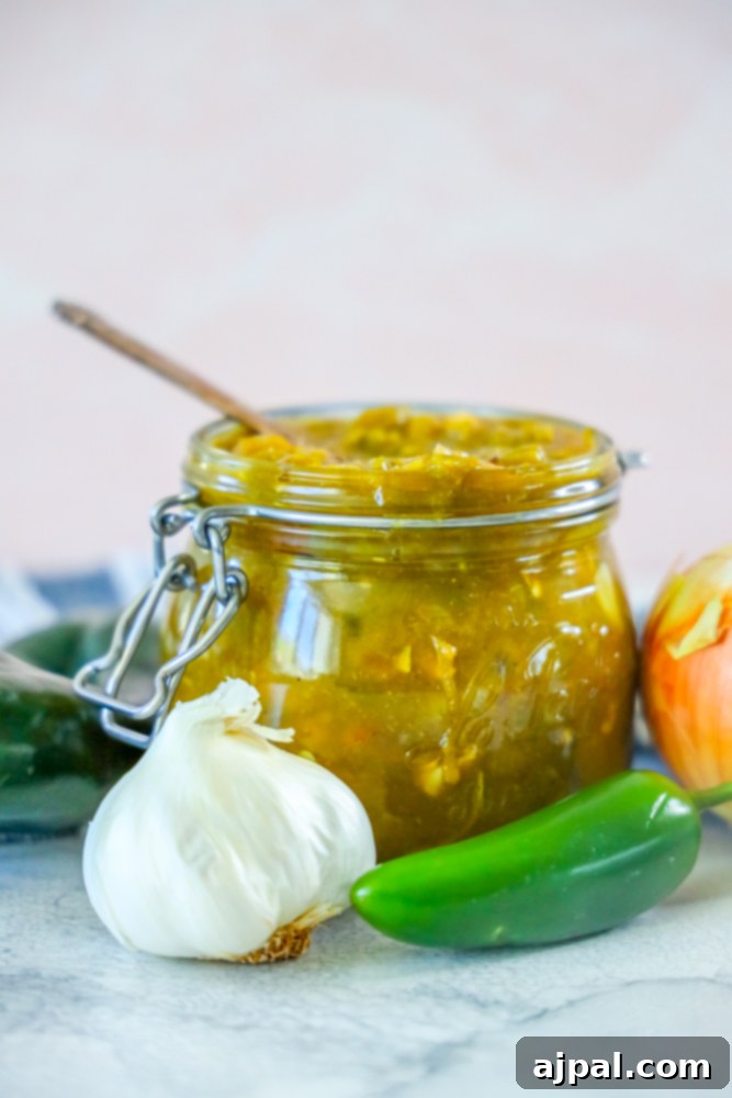 A beautifully presented jar of homemade green chile sauce, resting on a elegant marble table. Its vibrant green suggests freshness and rich flavor.