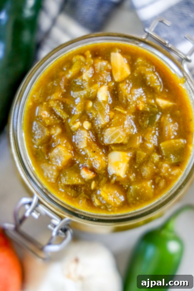 A vibrant jar of Colorado-style green chile sauce, showcasing its rich texture and color, set against a rustic background.