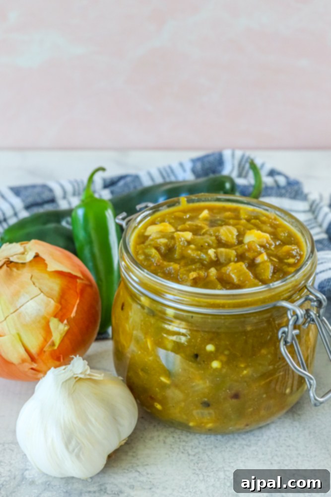 A jar of homemade green chile sauce beautifully arranged on a wooden table, surrounded by fresh garlic and onions, showcasing the ingredients used.