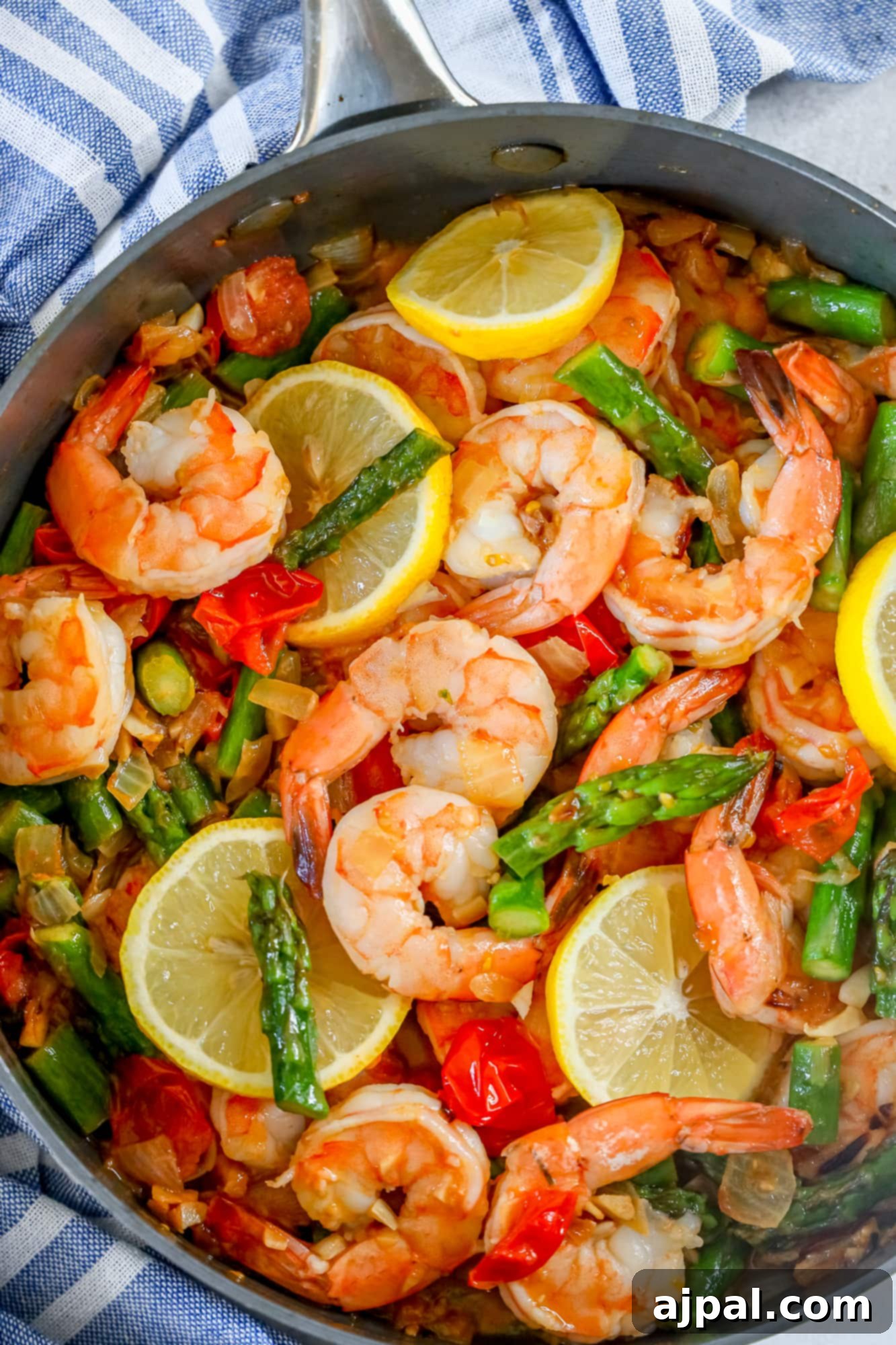 shrimp, asparagus, cherry tomatoes, and lemons in a grey skillet