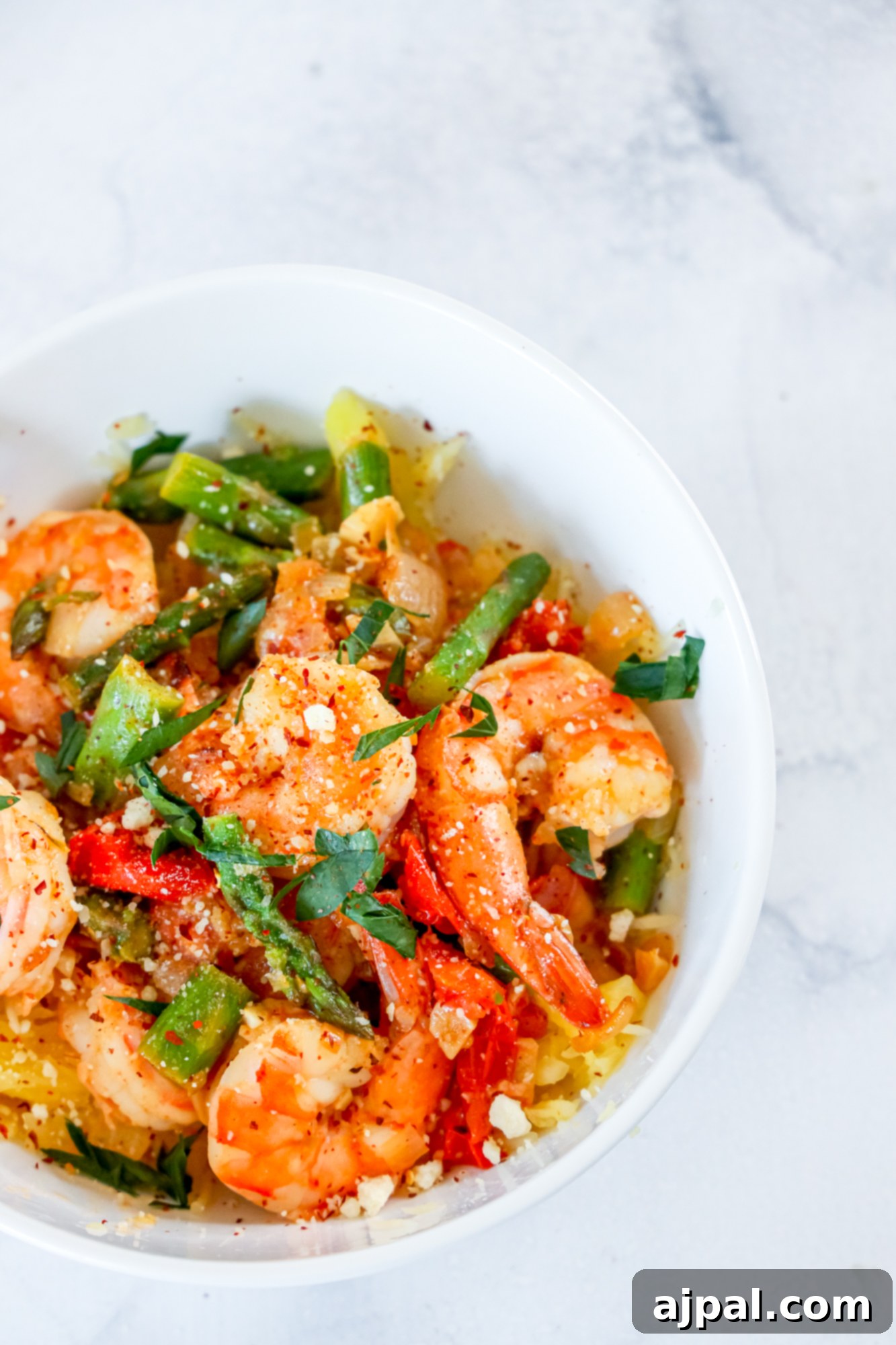 shrimp and asparagus over spaghetti squash noodles in a white bowl 