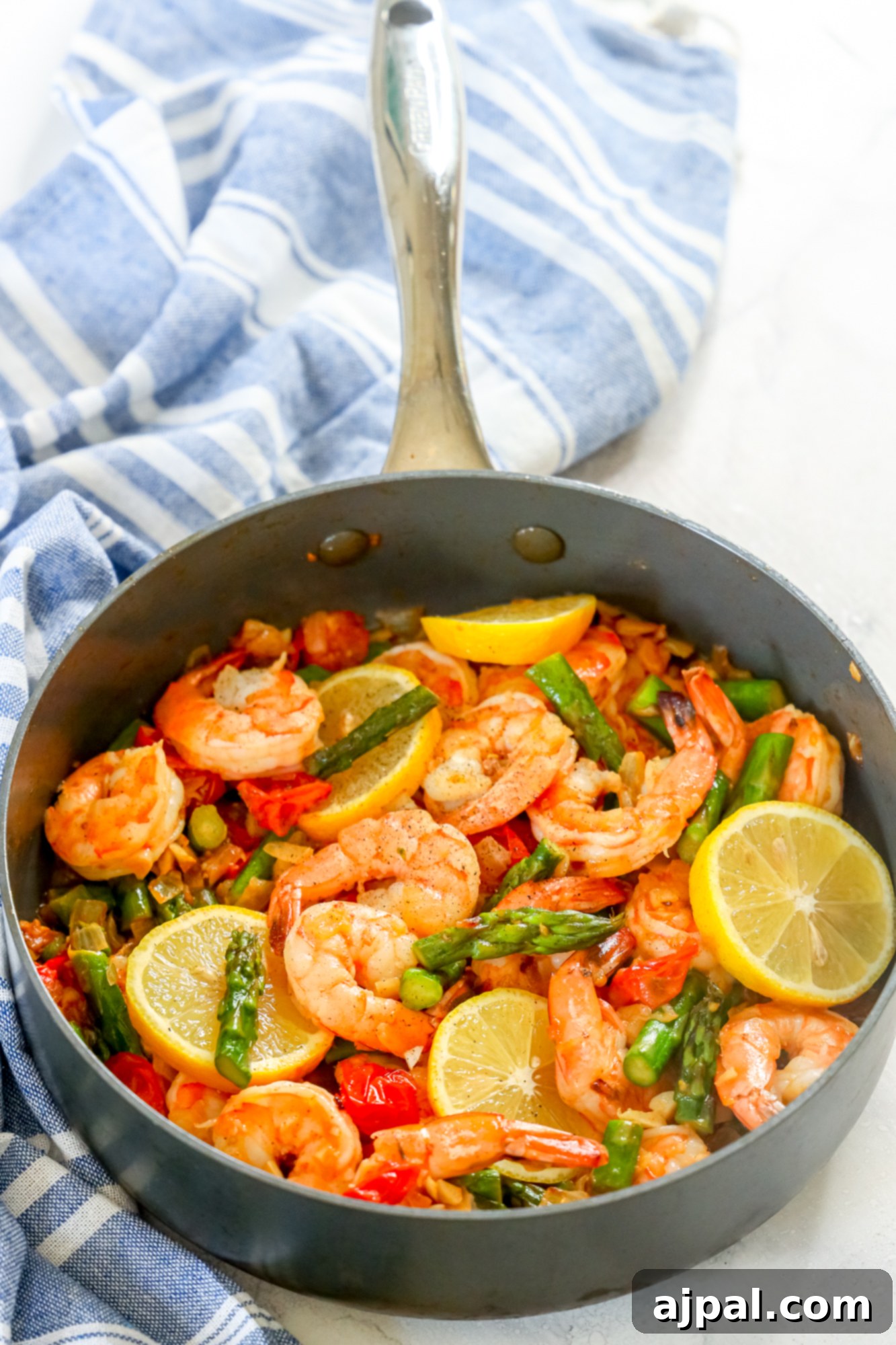 picture of shrimp, asparagus, cherry tomatoes, and lemons in a grey skillet