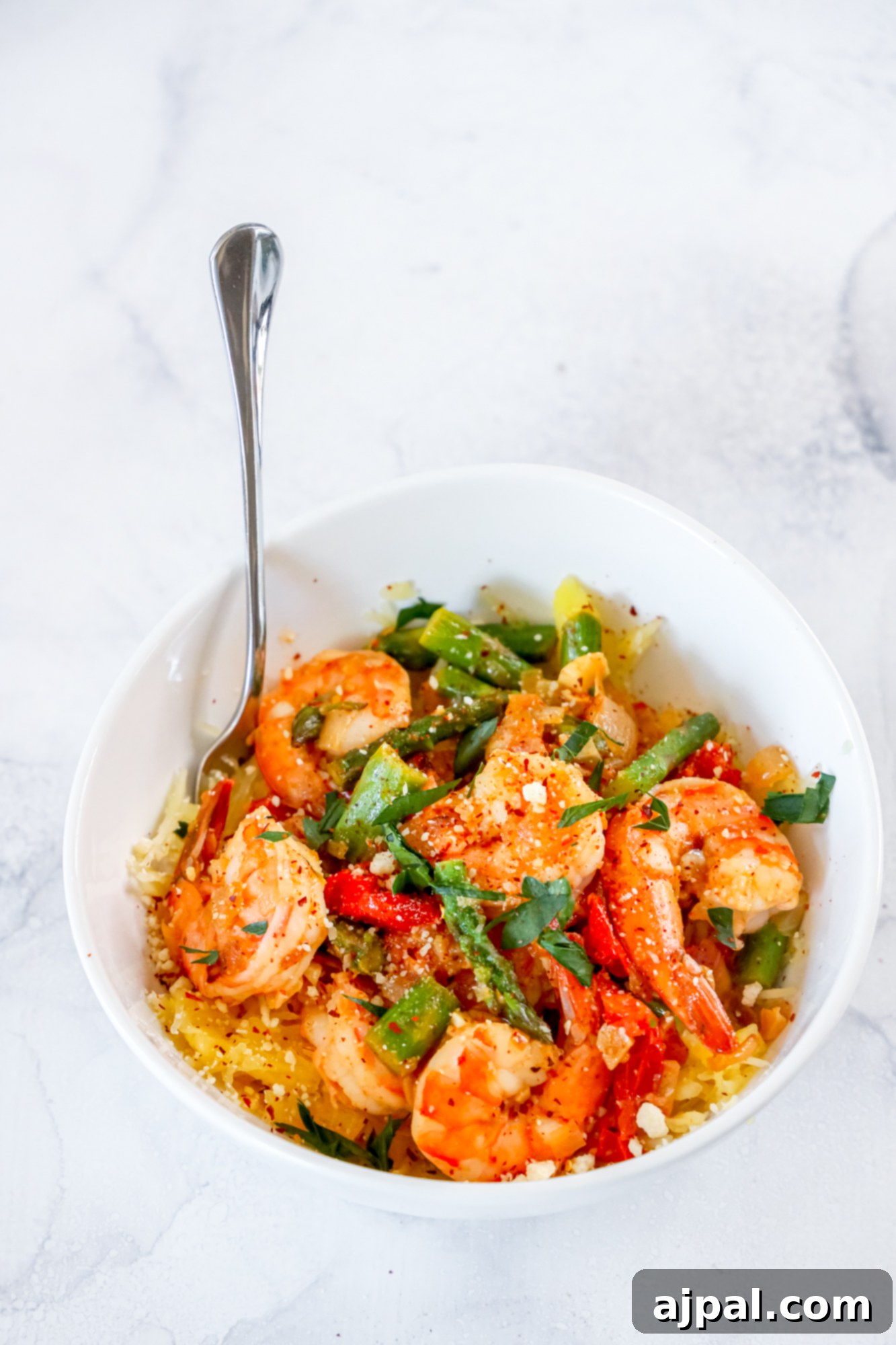 shrimp and asparagus over spaghetti squash noodles in a white bowl 