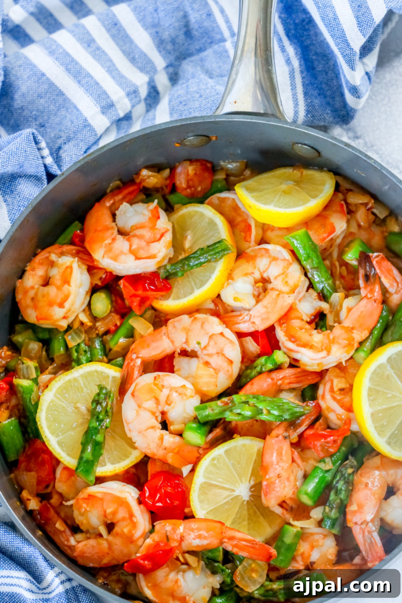 picture of shrimp, asparagus, cherry tomatoes, and lemons in a grey skillet