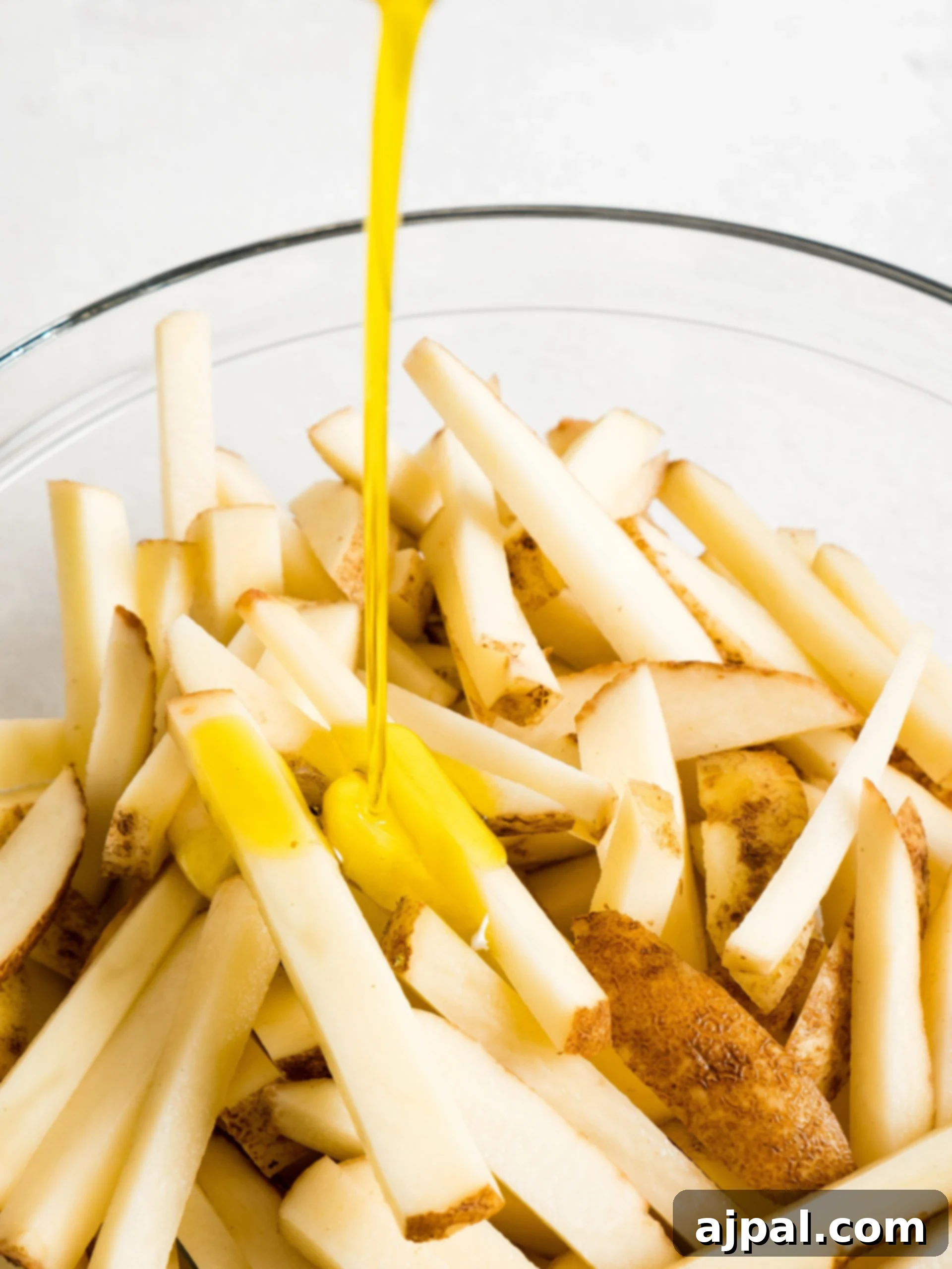 Olive oil being poured over potato sticks in a bowl.