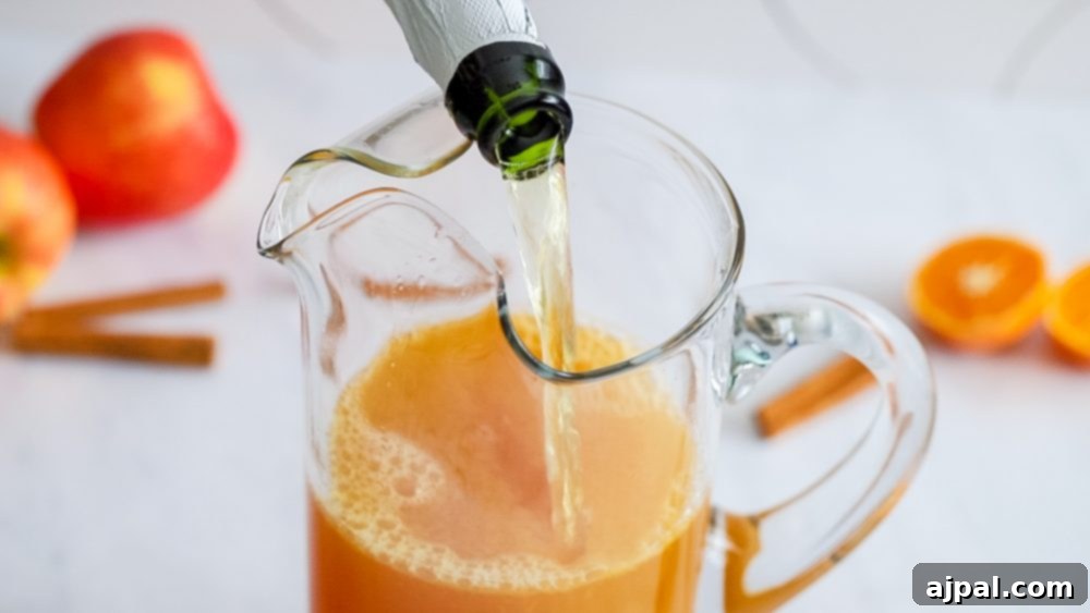 A stream of vibrant orange juice being poured into a clear pitcher, signifying the preparation of a refreshing Apple Rum Punch, highlighting the fresh ingredients.
