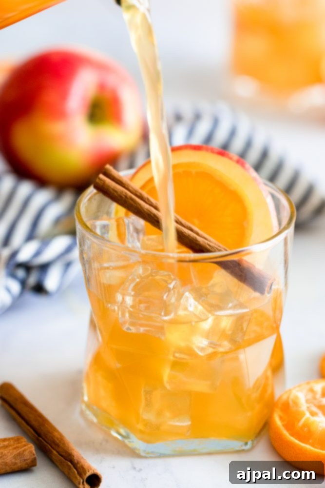 Pouring the rich orange-hued rum punch from a pitcher into a glass, garnished with cinnamon sticks and an orange slice, symbolizing the start of a refreshing drink.