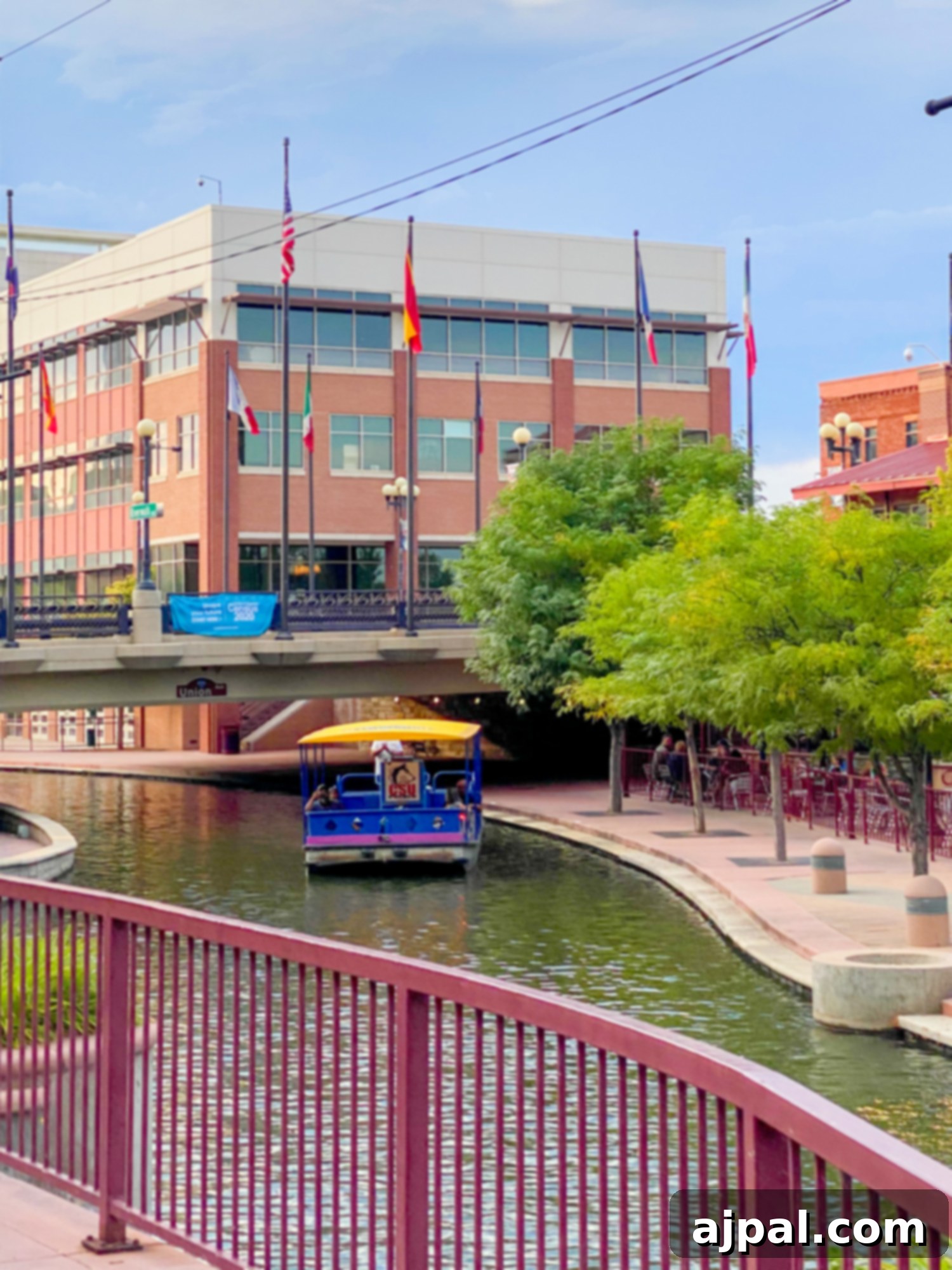 A charming boat cruises down the canal of the Pueblo Riverwalk, flanked by historic buildings.
