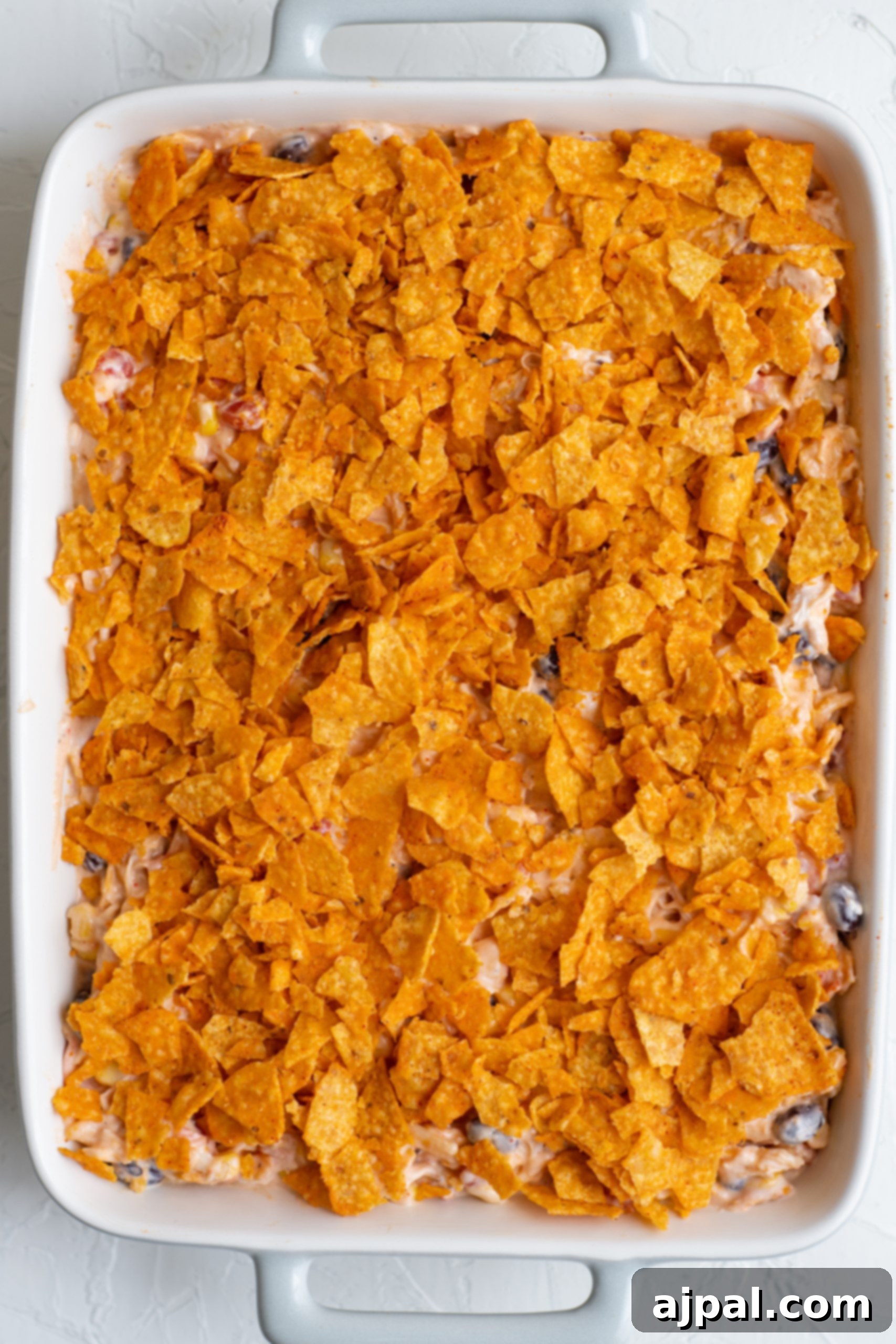 Crunchy Doritos Chicken Casserole 14 Cheesy nachos in a white baking dish topped with chicken and Doritos.