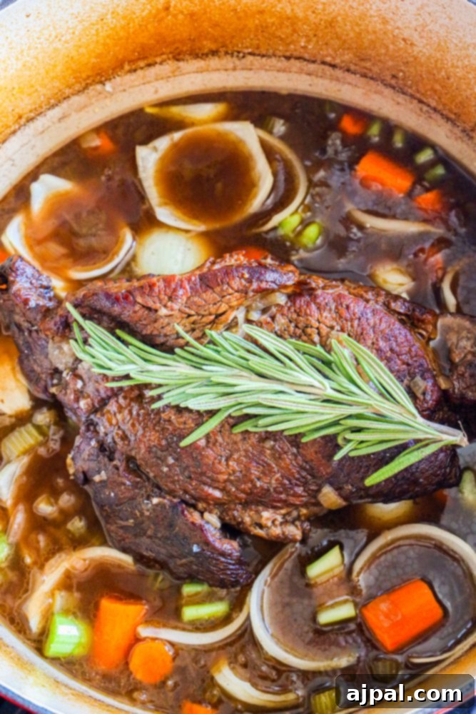 Fall-Apart Tender Pot Roast 3 A perfectly cooked pot roast in a Dutch oven, surrounded by rich gravy, tender carrots, celery, onions, and fresh rosemary sprigs.