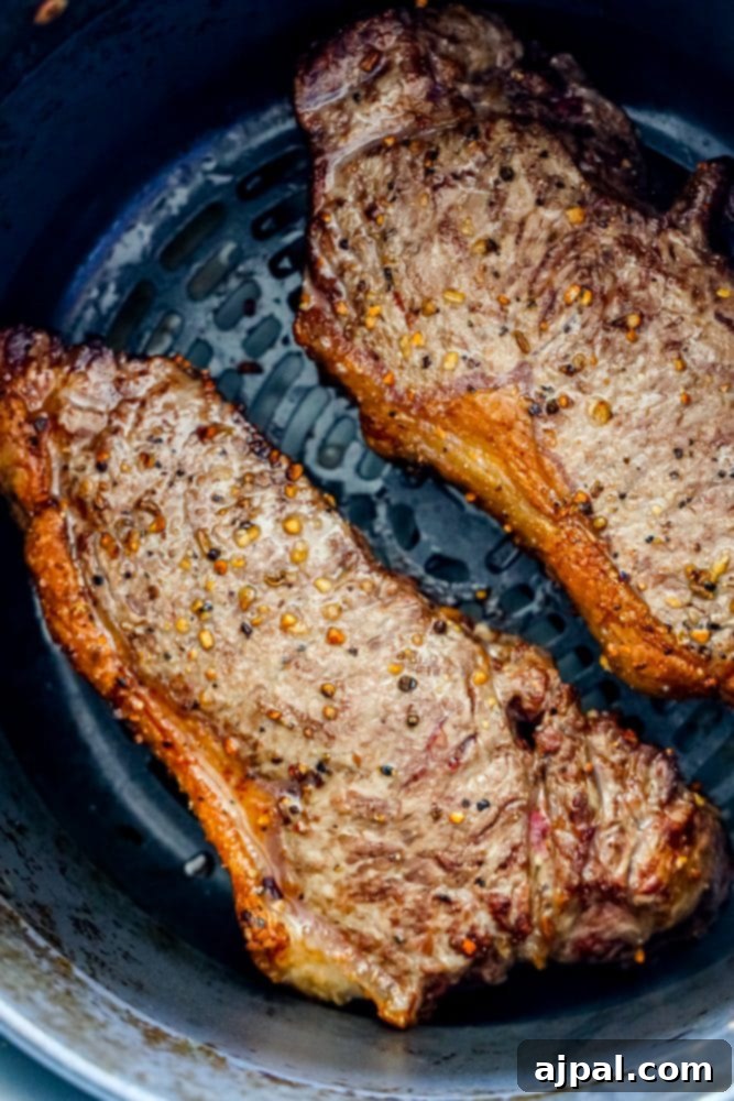 Master Your Air Fryer Steaks 2 Close-up of two perfectly cooked steaks with a golden-brown crust resting in an air fryer basket.