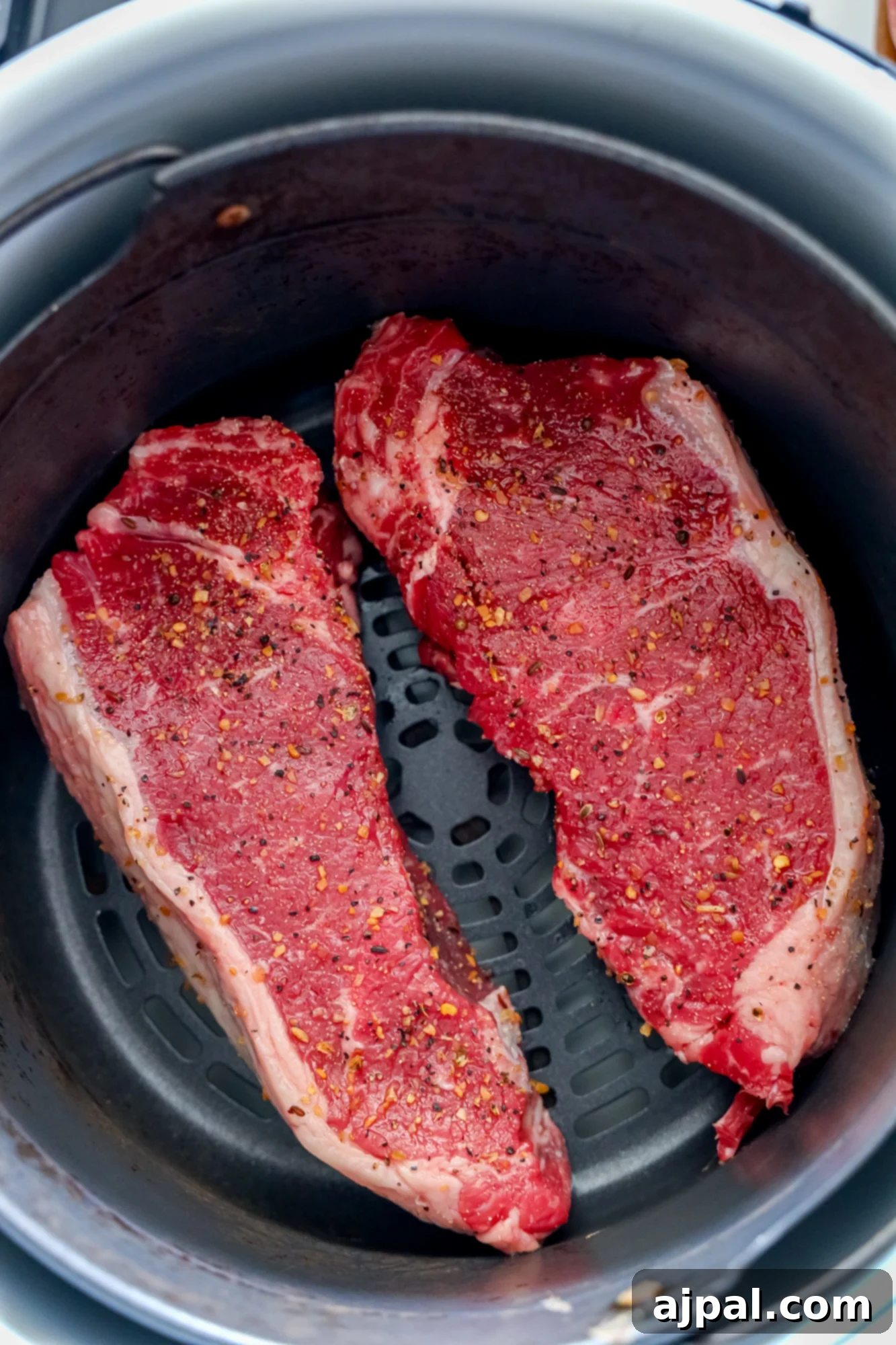 Master Your Air Fryer Steaks 6 Two seasoned steaks carefully placed inside an air fryer basket, ready for cooking.