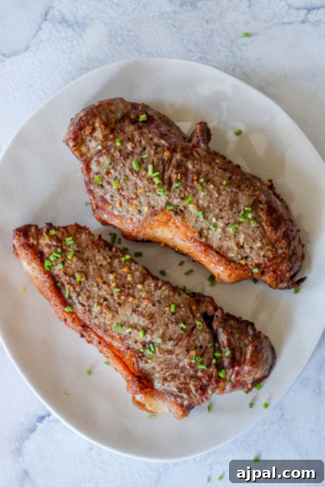 Master Your Air Fryer Steaks 9 Two air-fried steaks on a white plate, expertly sliced to reveal a perfect medium-rare interior, garnished with fresh chives.