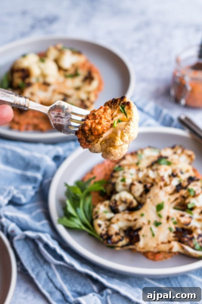 Effortless Cauliflower Steaks with Tangy Red Pepper Sauce 3 A hand holds a fork to a plate of perfectly grilled cauliflower steaks, generously drizzled with a rich red pepper sauce.