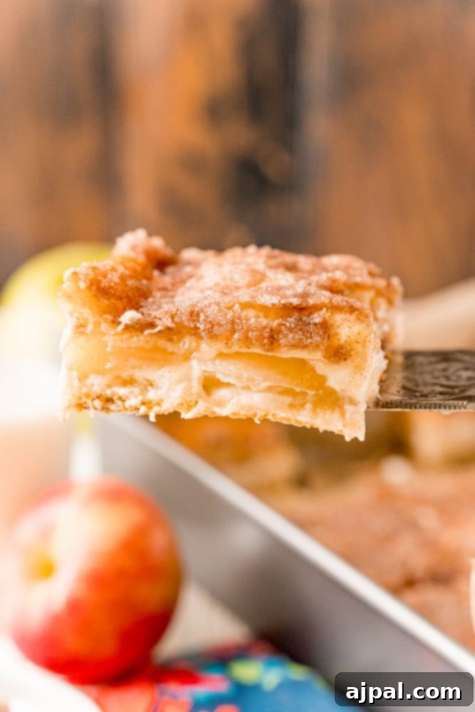 A slice of golden-brown apple sopapilla cheesecake bar with a fork, showing its creamy apple layers.