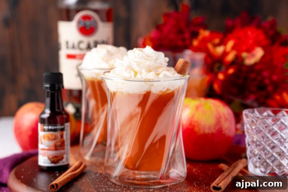 Two glasses of hot apple cider with whipped cream and cinnamon sticks.