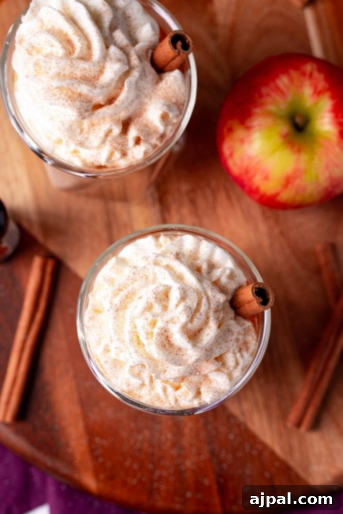 butter rum cider in a glass with whipped cream and cinnamon sticks