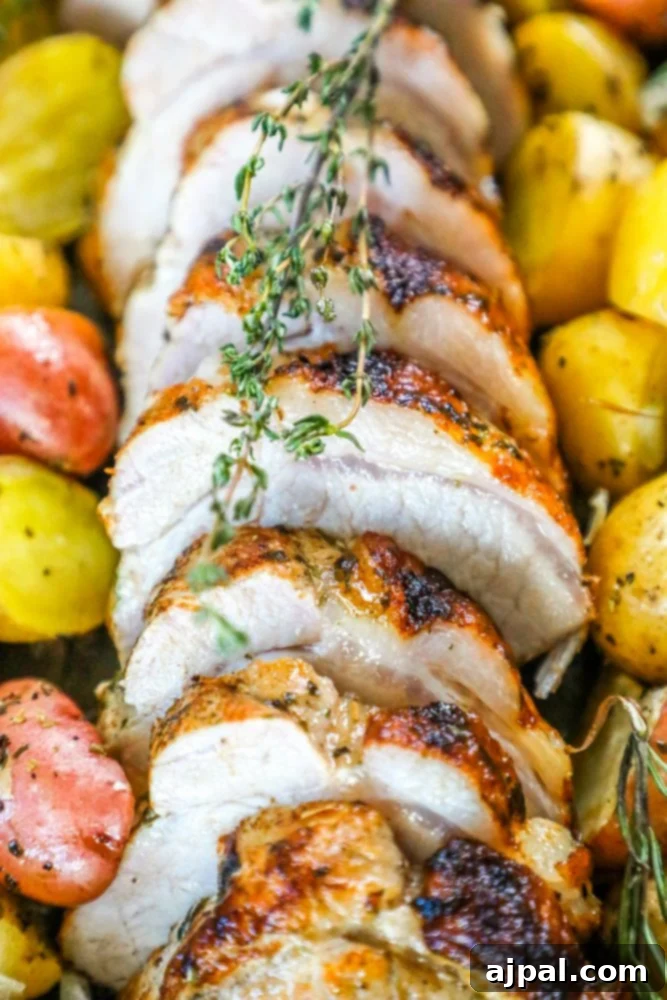 Close-up of baked pork loin and crispy roasted potatoes on a sheet pan, garnished with herbs.