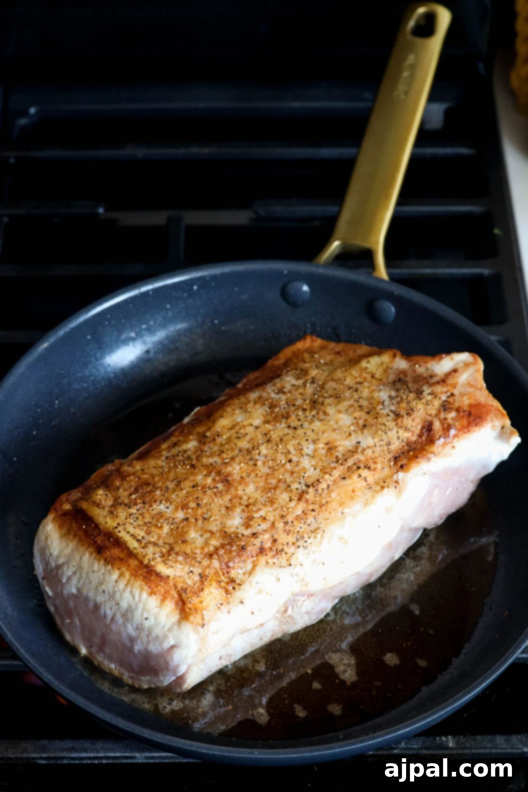 Pork loin searing in a hot pan, creating a golden-brown crust.